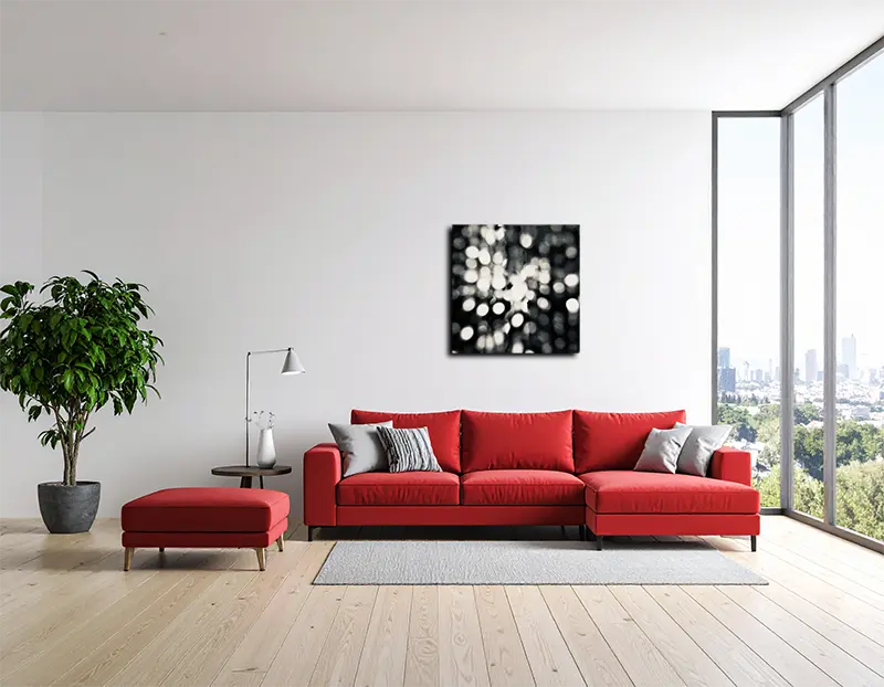 Das abstrakte quadratische Foto hängt an einer hellen wand hinter einem roten Sofa und einem Fenster von rechts