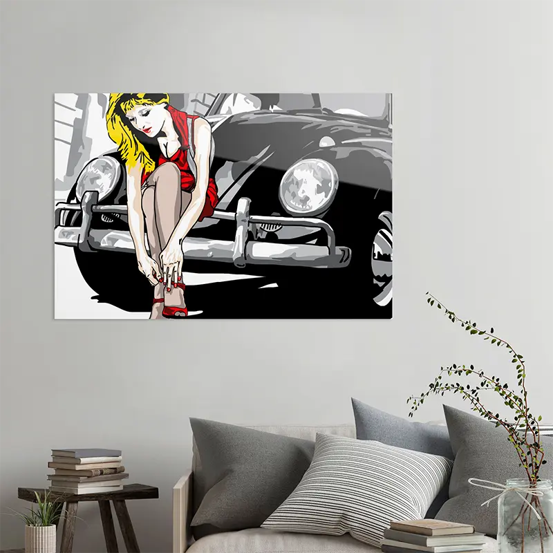 Frau mit rotem Kleid sitzt auf der Stoßstange eines schwarzen VW Käfers, an heller Wand hängend mit grauem Sofa