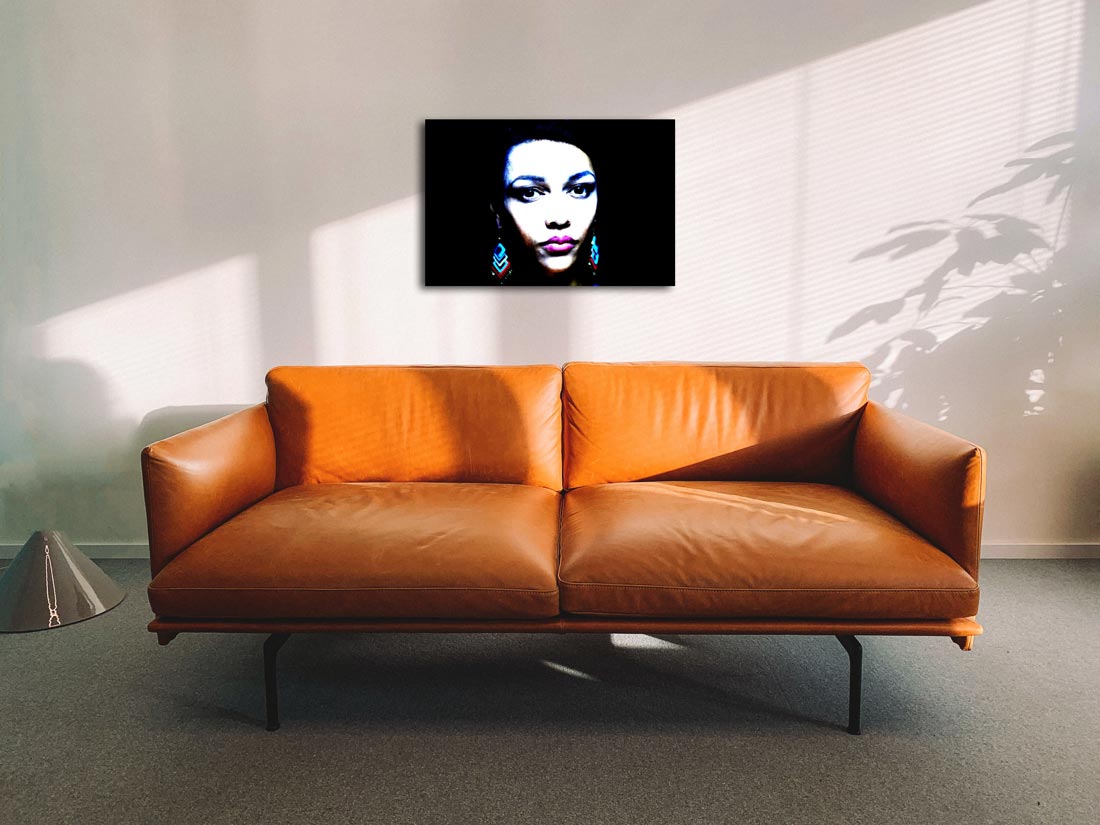 Das Portrait einer farbigen Frau mit farbigen Ohrringen, dunkler Hintergrund, an Wand hängend mit braunem Sofa