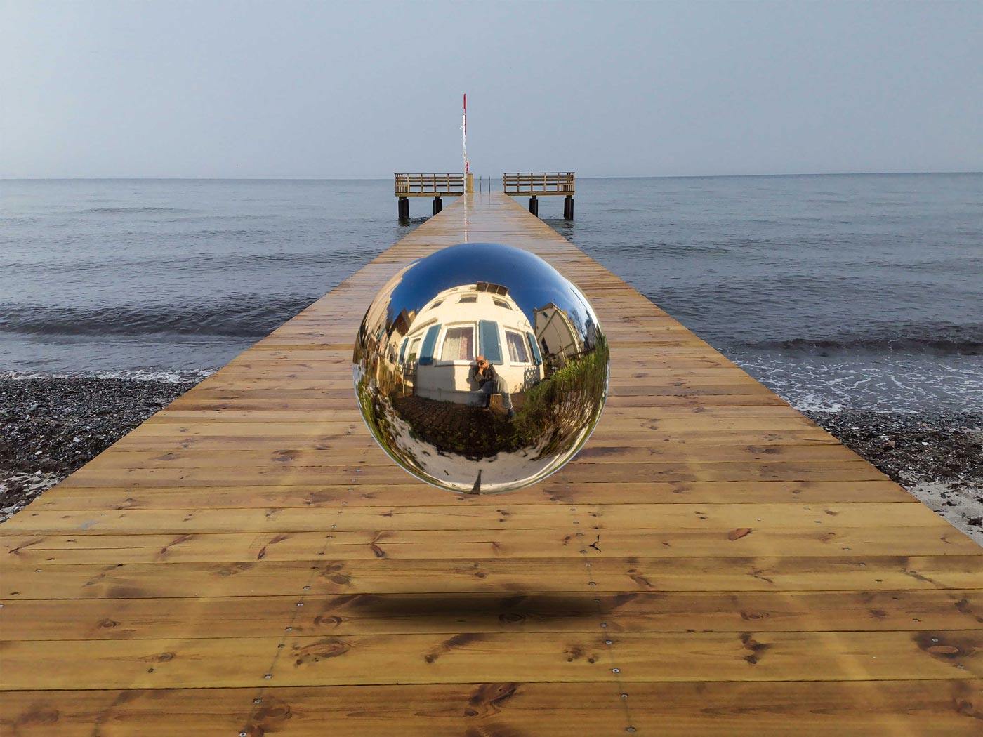 Eine Kugel schwebt über einem Steg der in die Ostsee führt-Surreales Werk