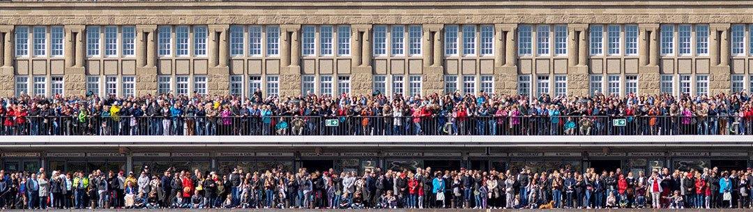 eine große Menschenmenge steht an einem Geländer und wartet auf etwas., Panoramabild