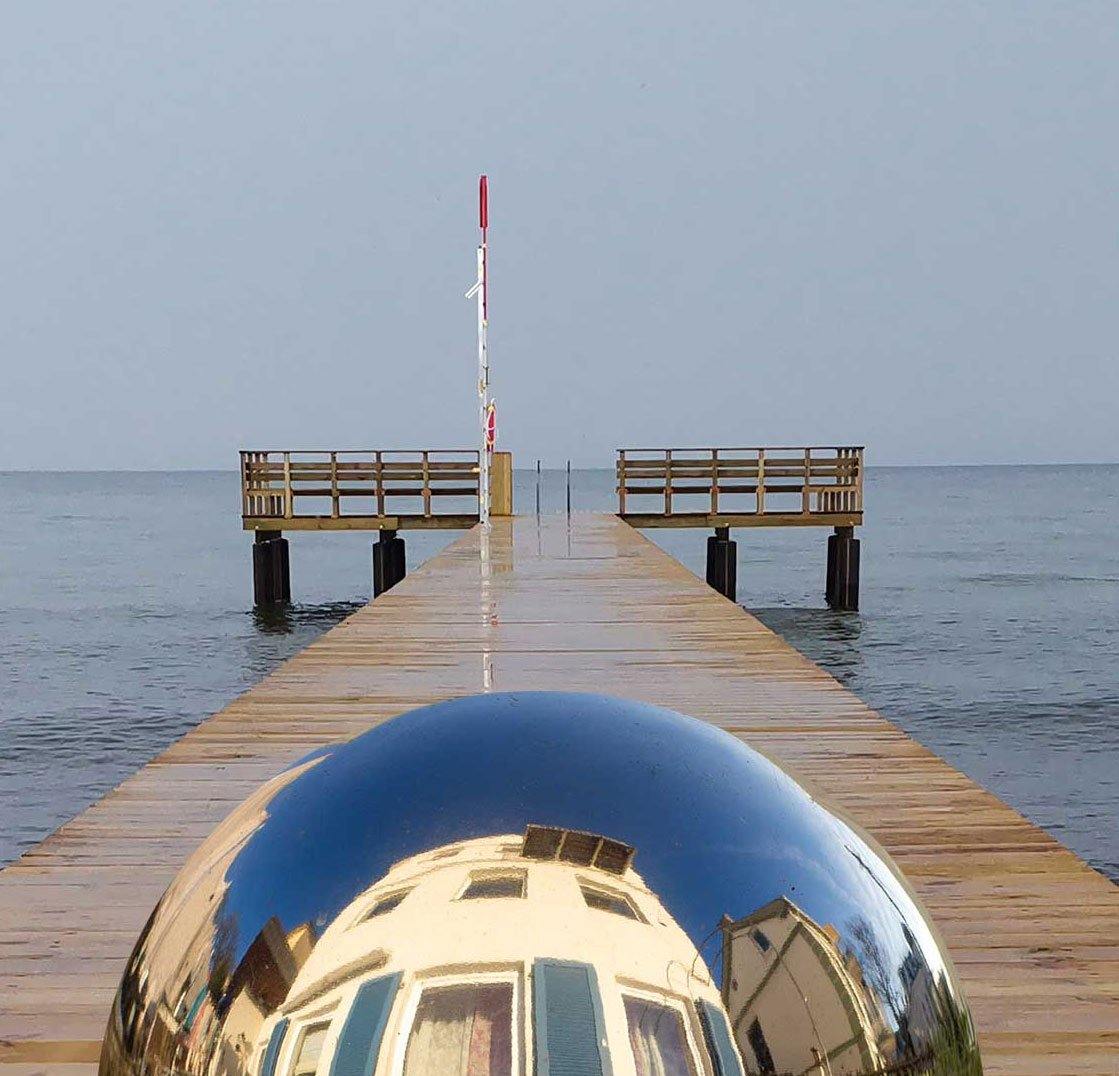 Eine Kugel schwebt über einem Steg der in die Ostsee führt-Surreales Werk. Details der Kugel und der See
