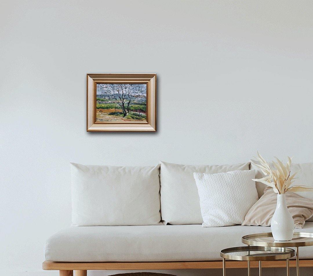 Impressionistisches Gemälde eines blühenden Baumes in einer Landschaft mit Häusern und Gras, goldener Rahmen, an heller Wand hängend mit weißem Sofa