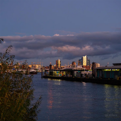 Farbfotografie des Hafens, das Abendlicht spiegelt sich in der Fassade der Elbphilharmonie, leichte Wolken am Himmel. Detailansicht mit Elbphilharmonie