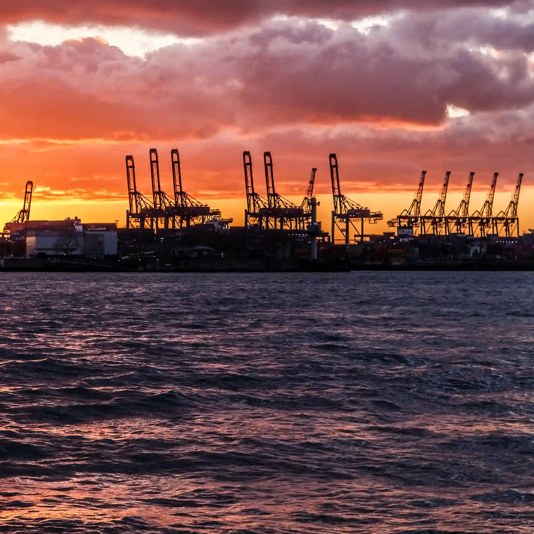 Farbfoto, orangefarbener Himmel, Hafenkräne im Schattenriss heben sich dunkel vor dem hellen Himmel ab, Detail mit hellem Himmel und Hafenkränen