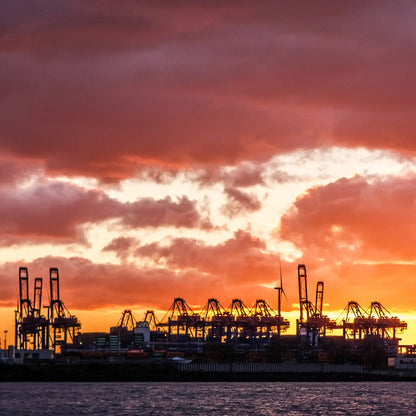 Farbfoto, orangefarbener Himmel, Hafenkräne im Schattenriss heben sich dunkel vor dem hellen Himmel ab, Detail mit hellem Himmel und dunklen Hafenkränen