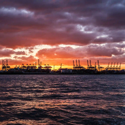 Farbfoto, orangefarbener Himmel, Hafenkräne im Schattenriss heben sich dunkel vor dem hellen Himmel ab