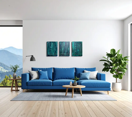 Drei Gemälde / Triptychon einer Serie in dunklem Grün an einer hellen Wand in einem modernen Wohnraum hängend, davor ein blaues Sofa